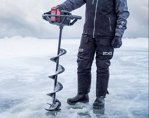 Guy ice fishing holding an ice fishing augers about to drill a hole, wearing FXR's Vapor Pro Tri-laminate Jacket and Pant