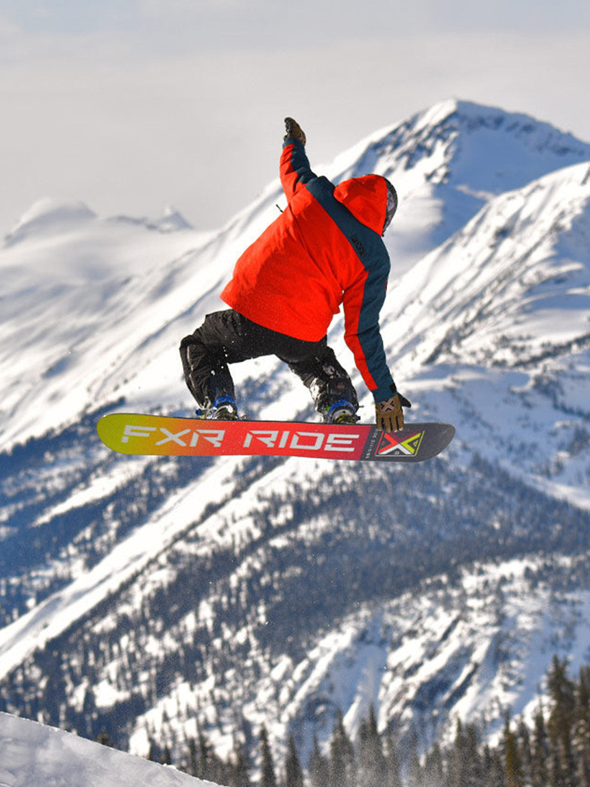Action image of a guy snowboarding on a mountain with FXR's Ride X collection