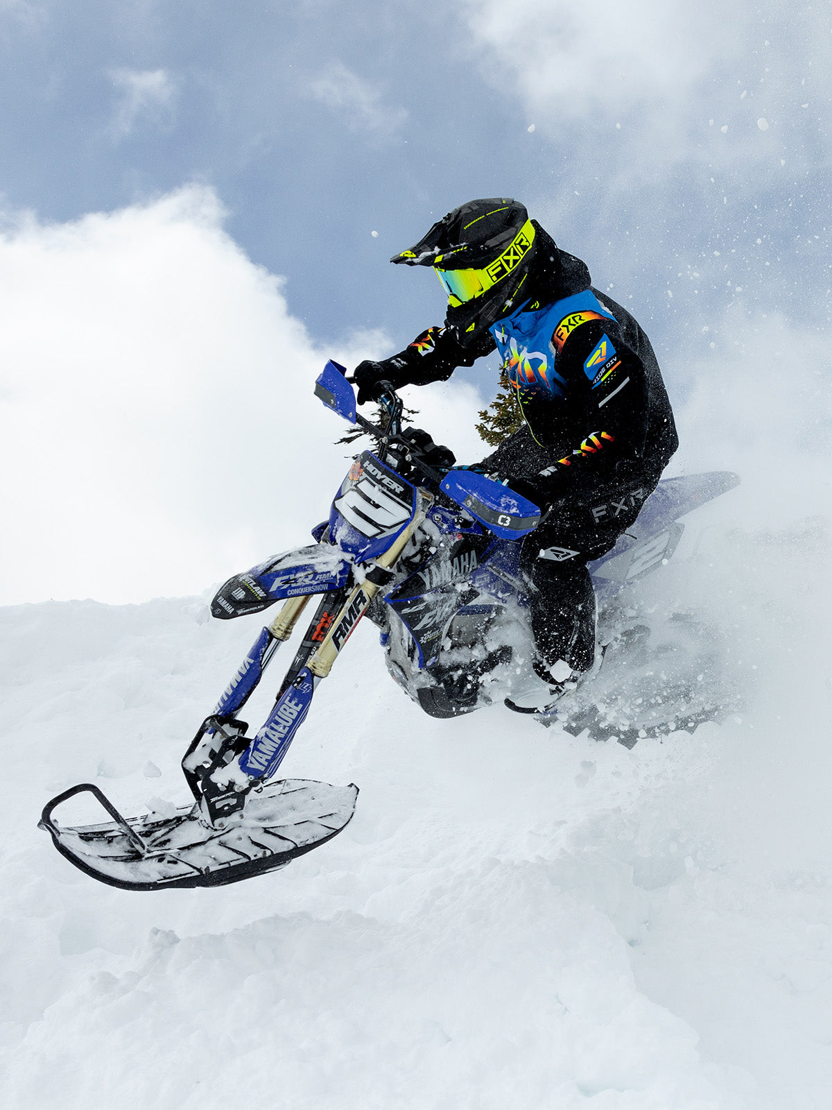 Action image of a guy snowmobiling on a mountain with FXR's Snow Bike collection