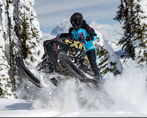 A guy standing on snowmobile wearing the FXR's Men's CX Lite Monosuit